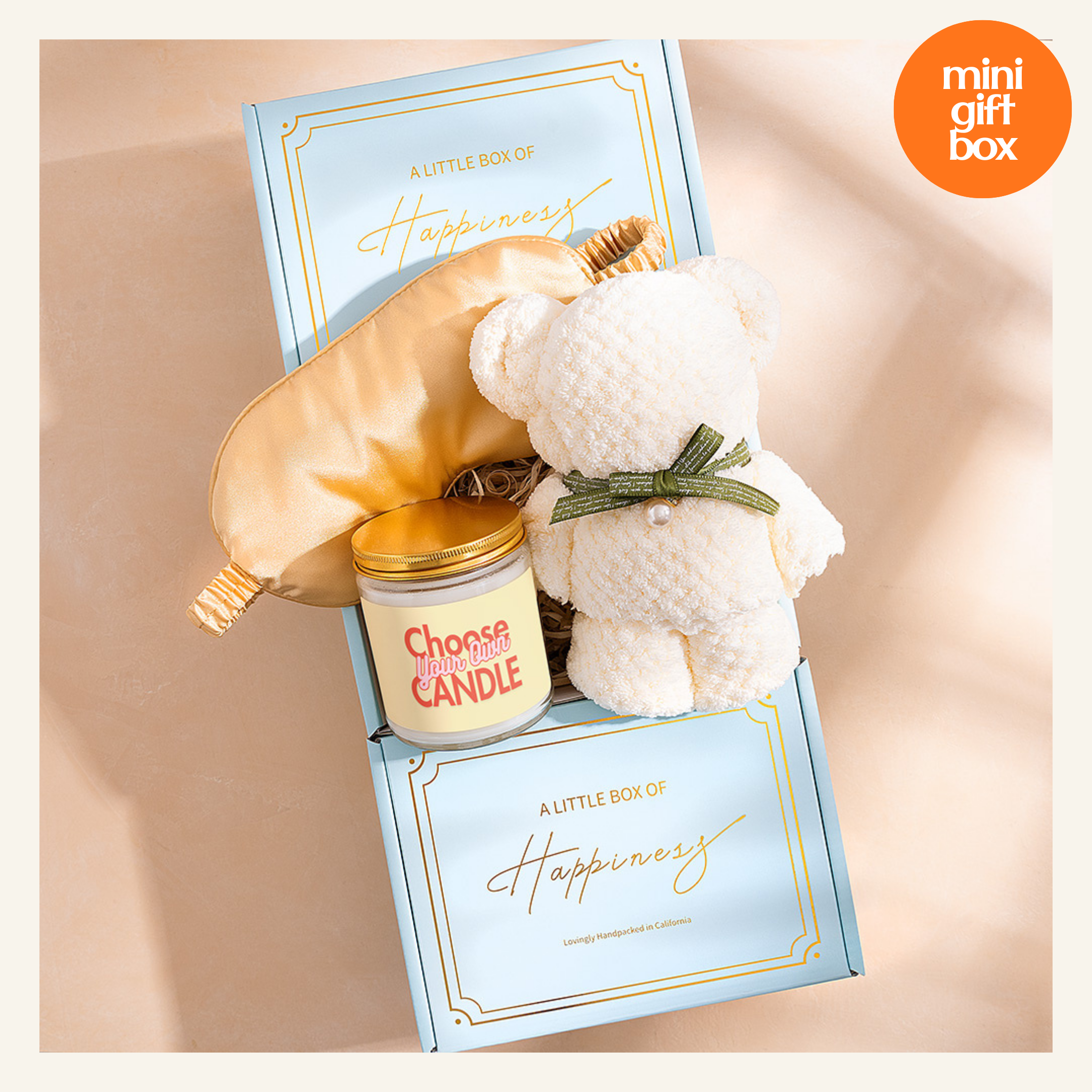 A gift box containing a white teddy bear, a gold-colored eye mask, and a candle labeled "Choose Your Candle".